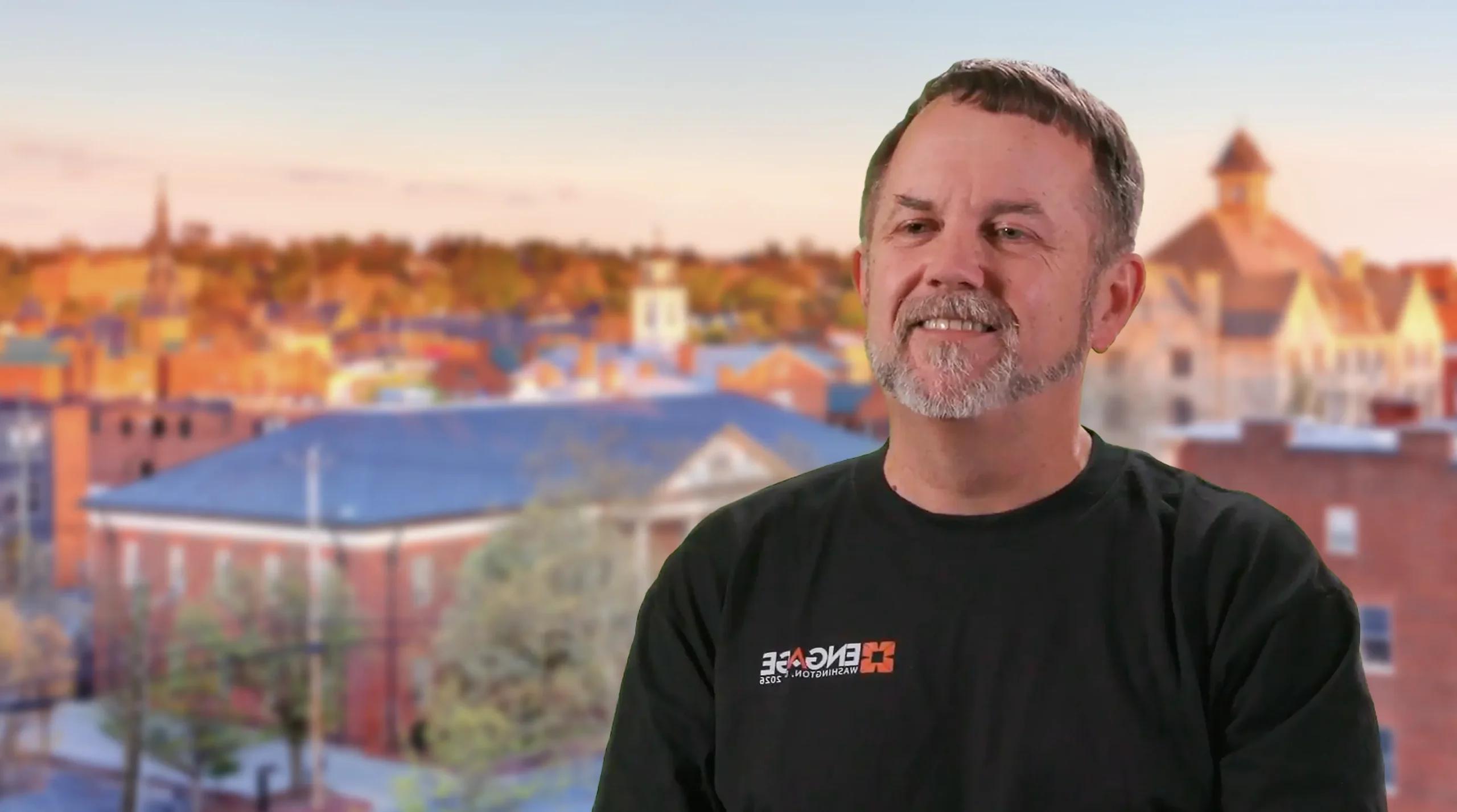 Bob Elliott smiling in front of a blurred small-town skyline at sunset.
